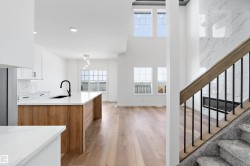 Open-concept layout with light wood-finish flooring, white cabinetry, and a kitchen island featuring a black sink and faucet - 