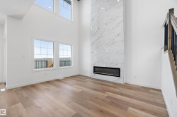 Double-height ceiling, wood-finish flooring, two large windows, two transom windows, and a linear electric fireplace with a marble-finish surround - 