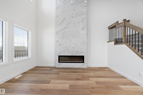 High ceilings, wood-finish flooring, full-height marble-look fireplace, linear electric fireplace, and a staircase with wood handrails and black metal spindles - 1763 Crossbill Loop Nw, Edmonton, AB - Indoor With Fireplace