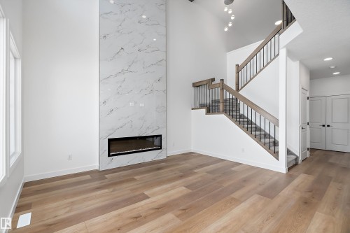 Two-story interior with wood-finish flooring, a linear electric fireplace with a marble-style surround, and a staircase with wood handrails and black metal balusters - 1763 Crossbill Loop Nw, Edmonton, AB - Indoor With Fireplace