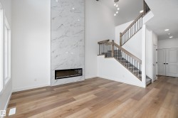 Two-story interior with wood-finish flooring, a linear electric fireplace with a marble-style surround, and a staircase with wood handrails and black metal balusters - 