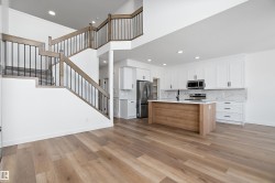 Open-concept living space with wood-finish flooring, a contemporary kitchen, and a prominent staircase with metal balusters - 
