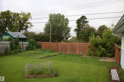 Expansive backyard featuring a manicured lawn, established wooden fencing, mature trees, a garden shed, and a raised planter bed - 4946 47 Street, Barrhead, AB - Outdoor With Backyard