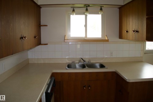 Kitchen featuring wood-finish cabinetry, white tile backsplash, a double basin stainless steel sink, and a window with natural light - 4946 47 Street, Barrhead, AB - Indoor Photo Showing Kitchen With Double Sink
