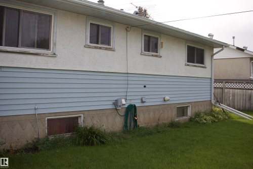 Exterior featuring stucco and light blue siding, multiple windows, a concrete foundation, and a grassy area - 4946 47 Street, Barrhead, AB - Outdoor With Exterior
