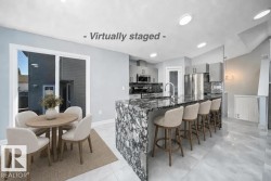Sleek kitchen with stainless steel appliances, a large island featuring a waterfall countertop, contemporary cabinetry, recessed lighting, and tile flooring - 