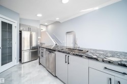 Kitchen featuring a stainless steel refrigerator, stainless steel dishwasher, light gray cabinetry, dark patterned countertop, and an undermount sink with a gooseneck faucet - 