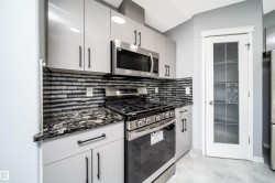 Kitchen featuring light grey cabinetry with dark hardware, stainless steel appliances, a tile backsplash, and patterned countertops - 