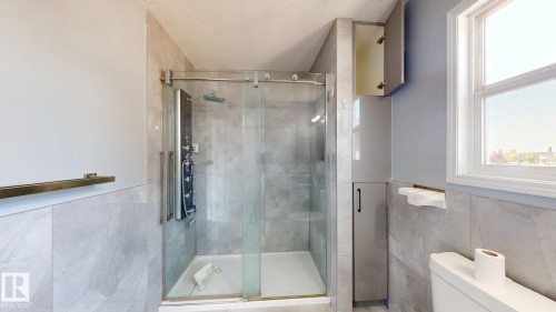 Tiled shower with sliding glass door, multi-function shower panel, and built-in storage cabinetry - 7848 7 Avenue Sw, Edmonton, AB - Indoor Photo Showing Bathroom