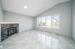 Vaulted ceiling with recessed lighting, large pane windows, stone-clad fireplace with mantel, and tile flooring - 