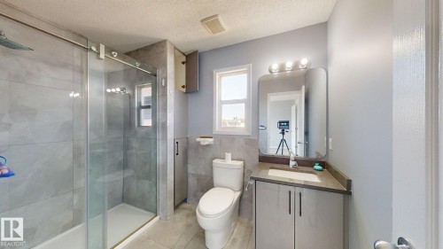 Bathroom featuring a glass-enclosed shower, single vanity with integrated sink, contemporary wall-mounted light fixture, and a window providing natural illumination - 7848 7 Avenue Sw, Edmonton, AB - Indoor Photo Showing Bathroom