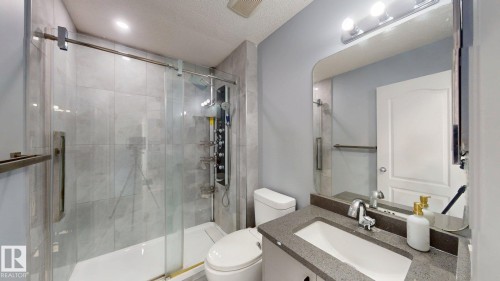 Glass-enclosed shower with tile surround, vanity with an integrated sink, broad wall mirror, and modern lighting fixture - 7848 7 Avenue Sw, Edmonton, AB - Indoor Photo Showing Bathroom