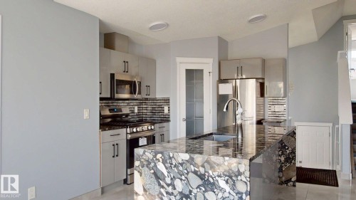 Gourmet kitchen with stainless steel appliances, sleek cabinetry, a natural stone island, and a tile backsplash - 7848 7 Avenue Sw, Edmonton, AB - Indoor Photo Showing Kitchen With Upgraded Kitchen
