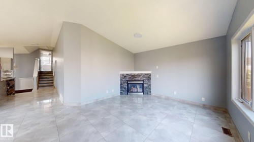 Spacious living area featuring large format tile flooring, a built-in electric fireplace with stone surround, a large window, and an integrated ceiling speaker - 7848 7 Avenue Sw, Edmonton, AB - Indoor Photo Showing Living Room With Fireplace