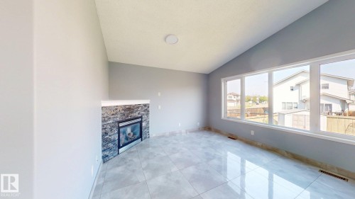 Vaulted ceiling, stone-surround fireplace, large pane windows, light grey paint, and tile flooring - 7848 7 Avenue Sw, Edmonton, AB - Indoor With Fireplace
