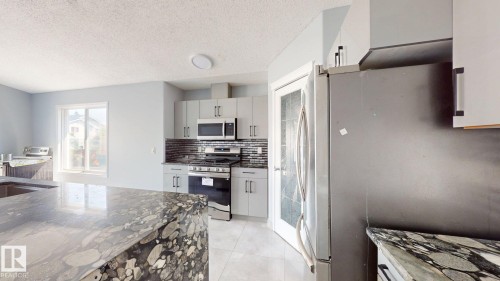 Kitchen featuring light-toned cabinetry, stainless steel appliances, dark subway tile backsplash, and light-toned tile flooring - 7848 7 Avenue Sw, Edmonton, AB - Indoor Photo Showing Kitchen