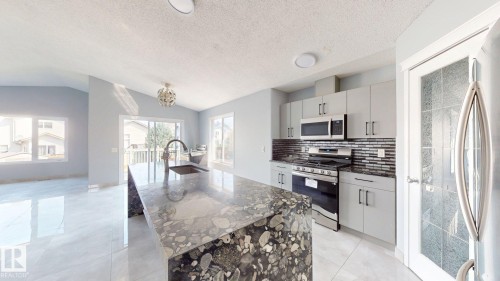 Kitchen featuring a waterfall island with an integrated sink, stainless steel appliances, grey cabinetry with dark hardware, and a dark tile backsplash - 7848 7 Avenue Sw, Edmonton, AB - Indoor Photo Showing Kitchen With Upgraded Kitchen