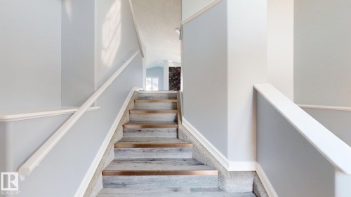 Staircase featuring wood-finish treads with metallic accents, carpeted risers, and white handrails - 7848 7 Avenue Sw, Edmonton, AB - Indoor Photo Showing Other Room