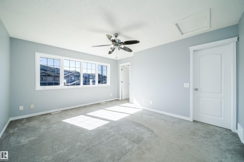 Spacious room featuring light gray carpeting, a multi-panel window with grid accents, a ceiling fan with light fixture, and a white paneled door - 7848 7 Avenue Sw, Edmonton, AB 