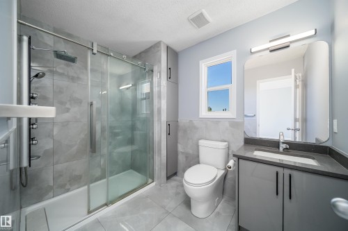 Bathroom featuring a glass-enclosed shower with a multi-function shower panel, contemporary vanity with an integrated sink, stone-finish countertop, and built-in storage cabinetry - 7848 7 Avenue Sw, Edmonton, AB 