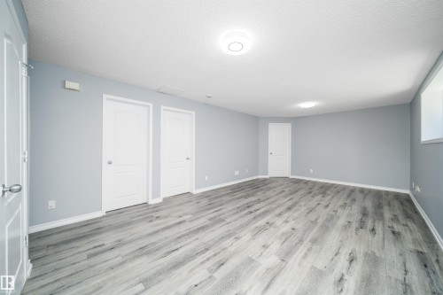 Spacious interior with light gray walls, wood-finish flooring, and multiple white panel doors - 7848 7 Avenue Sw, Edmonton, AB 