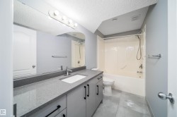 Spacious bathroom featuring a single vanity with stone-finish countertop, integrated sink, and contemporary cabinetry with black hardware - 