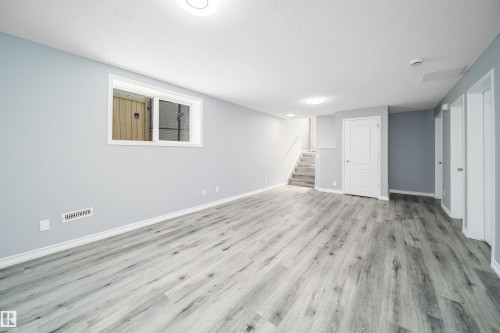 Expansive open area with wood-finish flooring, recessed lighting, and a window with security bars - 7848 7 Avenue Sw, Edmonton, AB 