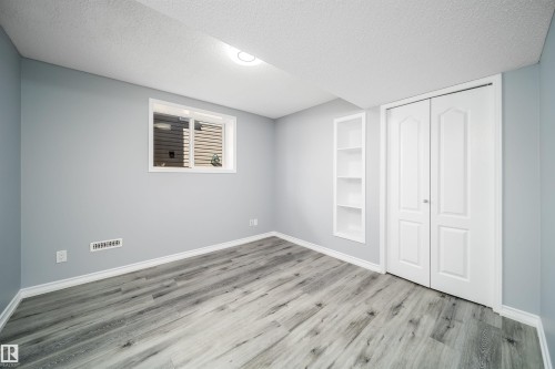 Wood-finish flooring, recessed built-in shelving, white bi-fold closet doors, and a window with white trim - 7848 7 Avenue Sw, Edmonton, AB 