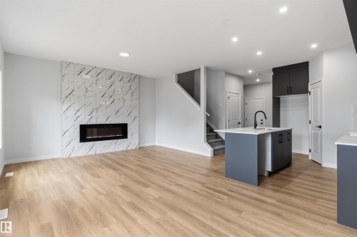 Open concept living space featuring wood-finish flooring, a contemporary fireplace with a tiled surround, recessed lighting, and a kitchen island with integrated sink - 8815 181 Avenue Nw, Edmonton, AB - Indoor With Fireplace