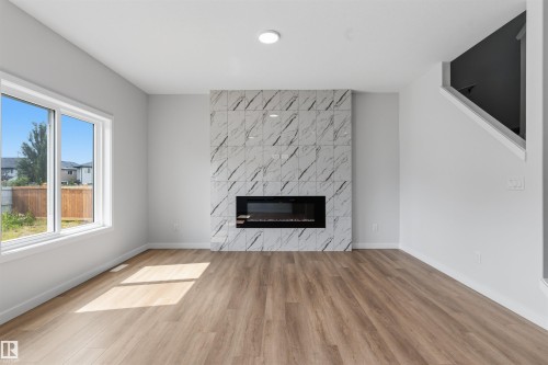 Wood-finish flooring, white walls, and a modern linear fireplace with a patterned tile surround - 8815 181 Avenue Nw, Edmonton, AB - Indoor Photo Showing Living Room With Fireplace