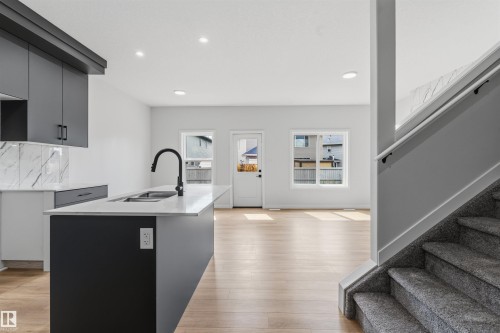 Modern kitchen with matte gray cabinetry, kitchen island with integrated sink, light-toned wood-finish flooring, and recessed lighting - 8815 181 Avenue Nw, Edmonton, AB - Indoor Photo Showing Kitchen