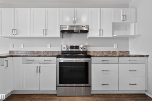White shaker-style cabinetry with brushed nickel hardware, stainless steel electric range, stainless steel range hood, and wood-finish flooring - 1816 36 Avenue Nw, Edmonton, AB - Indoor Photo Showing Kitchen