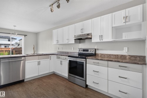 Bright kitchen featuring stainless steel appliances, white cabinetry with dark hardware, brown wood-finish flooring, and a sliding glass door - 1816 36 Avenue Nw, Edmonton, AB - Indoor Photo Showing Kitchen
