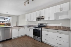 Bright kitchen featuring stainless steel appliances, white cabinetry with dark hardware, brown wood-finish flooring, and a sliding glass door - 