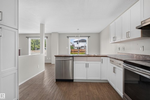 White shaker cabinetry, wood-finish flooring, stainless steel dishwasher, integrated sink, and dark countertops - 1816 36 Avenue Nw, Edmonton, AB - Indoor Photo Showing Kitchen