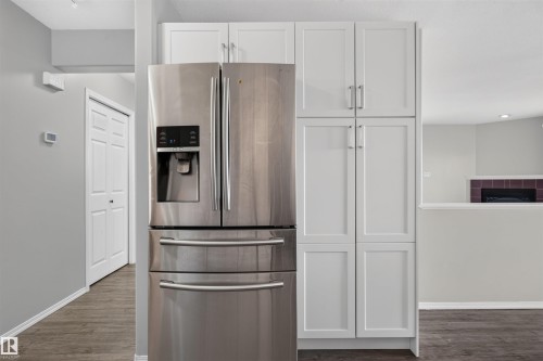Stainless steel French door refrigerator, white shaker-style cabinetry, wood-finish flooring, and a built-in fireplace feature - 1816 36 Avenue Nw, Edmonton, AB - Indoor