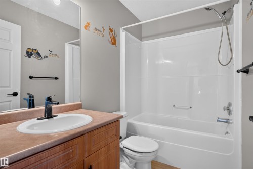 Bathroom featuring a single-sink vanity with wood-finish cabinetry, a white oval undermount sink, and a combination tub and shower with a handheld showerhead - 1816 36 Avenue Nw, Edmonton, AB - Indoor Photo Showing Bathroom