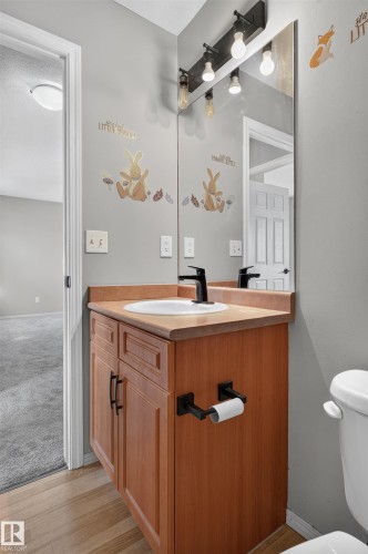 Wood-finish flooring with a vanity featuring a black faucet and a wall-mounted light fixture - 1816 36 Avenue Nw, Edmonton, AB - Indoor Photo Showing Bathroom
