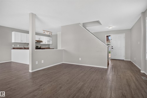 Wood-finish flooring throughout, complemented by a contemporary kitchen featuring white cabinetry and a stainless steel sink - 1816 36 Avenue Nw, Edmonton, AB - Indoor Photo Showing Other Room