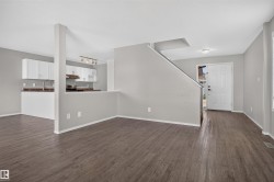 Wood-finish flooring throughout, complemented by a contemporary kitchen featuring white cabinetry and a stainless steel sink - 