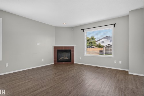 Wood-finish flooring, corner fireplace with red tile surround, recessed lighting, and a large window with blinds - 1816 36 Avenue Nw, Edmonton, AB - Indoor Photo Showing Living Room With Fireplace