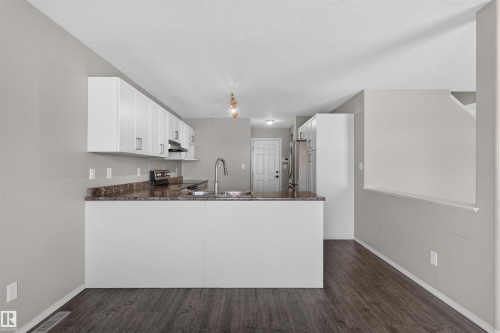 Kitchen featuring white cabinetry, a peninsula with a stainless steel sink, wood-finish flooring, and light-toned walls - 1816 36 Avenue Nw, Edmonton, AB - Indoor Photo Showing Kitchen