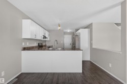 Kitchen featuring white cabinetry, a peninsula with a stainless steel sink, wood-finish flooring, and light-toned walls - 