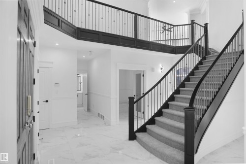 Two-story foyer featuring an elegant curved staircase with carpeted treads, dark wood newel posts, and wrought iron balusters - 6823 18 Avenue Sw, Edmonton, AB - Indoor Photo Showing Other Room