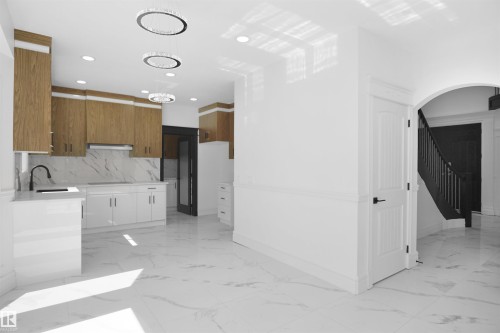 Expansive open-concept space featuring marble-look flooring, white cabinetry, wood-finish upper cabinetry, and contemporary chandeliers - 6823 18 Avenue Sw, Edmonton, AB - Indoor Photo Showing Kitchen