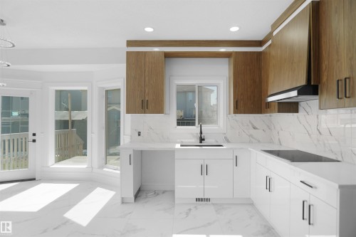 Modern kitchen featuring white cabinetry, wood-finish upper cabinets, a built-in cooktop, and a white tile backsplash - 6823 18 Avenue Sw, Edmonton, AB - Indoor Photo Showing Kitchen With Upgraded Kitchen