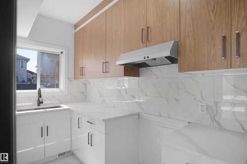 Modern kitchen featuring wood-finish upper cabinetry, white lower cabinetry, white countertops, and a white tile backsplash - 6823 18 Avenue Sw, Edmonton, AB - Indoor