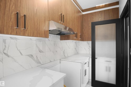Contemporary kitchen featuring wood-finish cabinetry, white countertops, a stainless steel range hood, and a black-framed door with textured glass - 6823 18 Avenue Sw, Edmonton, AB - Indoor Photo Showing Laundry Room
