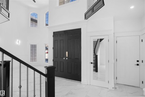 Grand entryway featuring a double-height ceiling, large arched windows, white marble-finish flooring, a dark wood double-door entry, and a dark wood staircase with wrought iron balusters - 6823 18 Avenue Sw, Edmonton, AB - Indoor Photo Showing Other Room