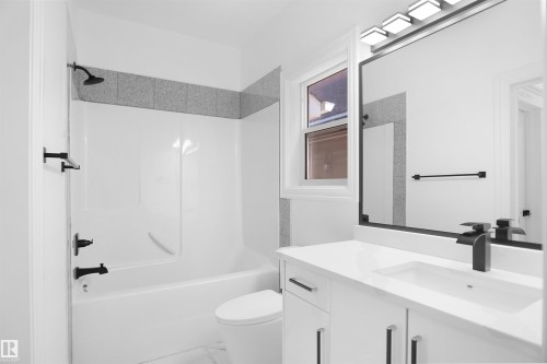 White vanity with integrated sink, black matte faucet, framed mirror, and a white tub with shower - 6823 18 Avenue Sw, Edmonton, AB - Indoor Photo Showing Bathroom